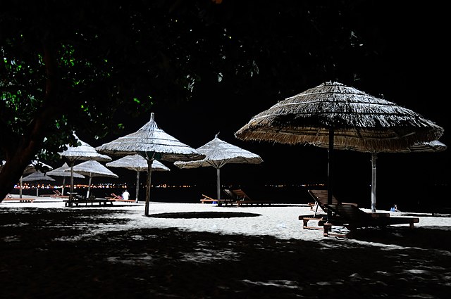 spiaggia di notte con ombrelloni di paglia lettini e stelle cadenti ideale per bagno di mezanotte