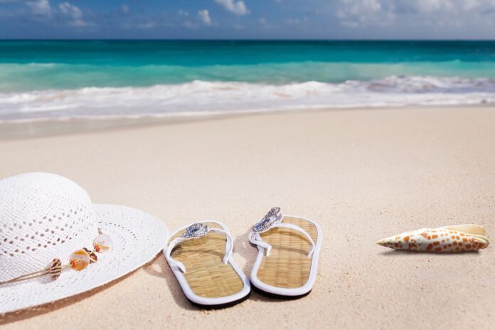 Vacanze ad agosto - un cappello di paglia a falda larga, un paio di ciabatte infradito e una stella marina appogiate sulla sabbia di una spiaggia di fronte al mare