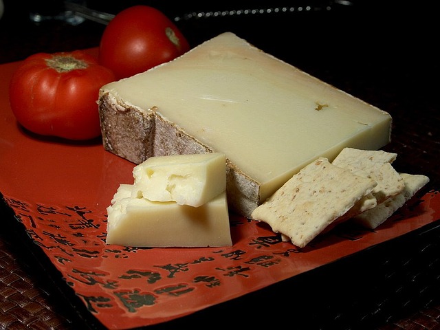 una fetta di fontina con dei pezzi di formaggio vicini, appoggiati su un tovagliolo rosso e dei pomodori