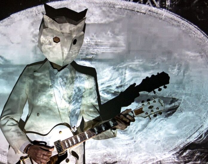 un uomo con un sacchetto di carta in testa, a forma di gatto, con i fori per gli occhi, sta suonando la chitarra e dietro di lui una grandissima luna. E' un disegno