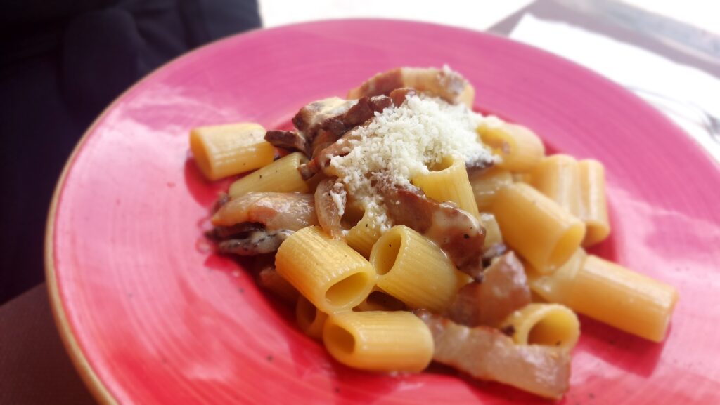 La carbonara - un piatt rosso con dentro una porzione di pasta con guanciale e pecorino spolverato sopra i maccheroni