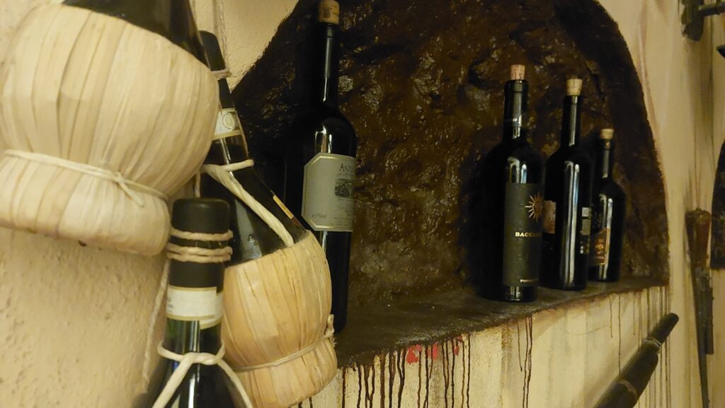 cucina romana Antica Osteria Rugantino Trastevere Roma - una parete con un anicchia a semicerchio dove sono esposte delle bottiglie di vino e sul muro ci sono anche dei fiaschi di vino impagliati