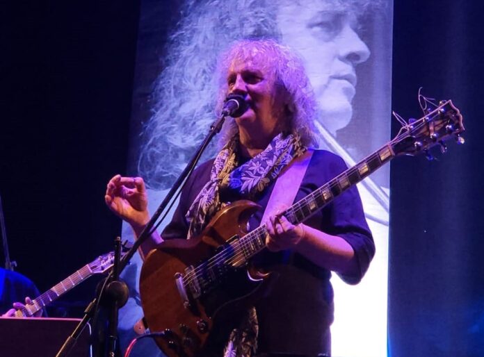 memorie di un capellone - gianfranco caliendo in primo piano, durante un concerto, a tracolla una chitarra elettrica