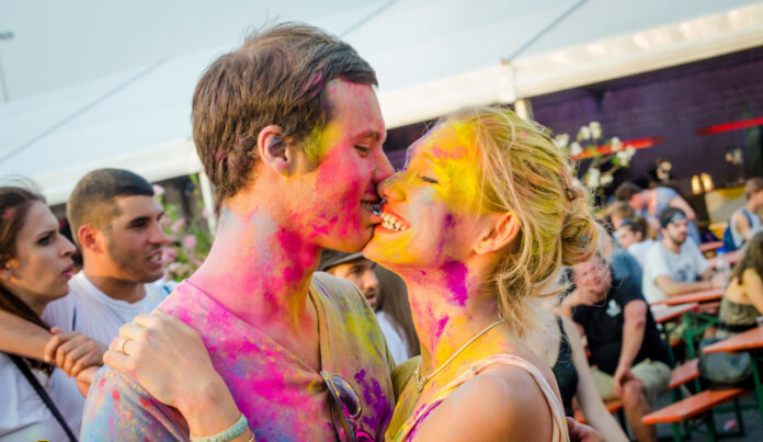 Festival dei colori - un ragazzo e una ragazza si baciano . Sono coperti di colori e intorno a loro c'è una grossa folla sporca di colori
