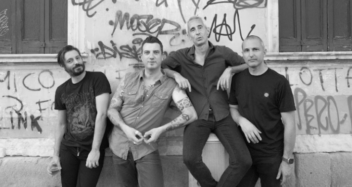 la santeria - i quattro componenti la band, in piedi davanti a un muro coperto di graffiti