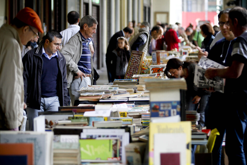 molte peronse sfogliano libri su una bancarella sotto i portici di torino