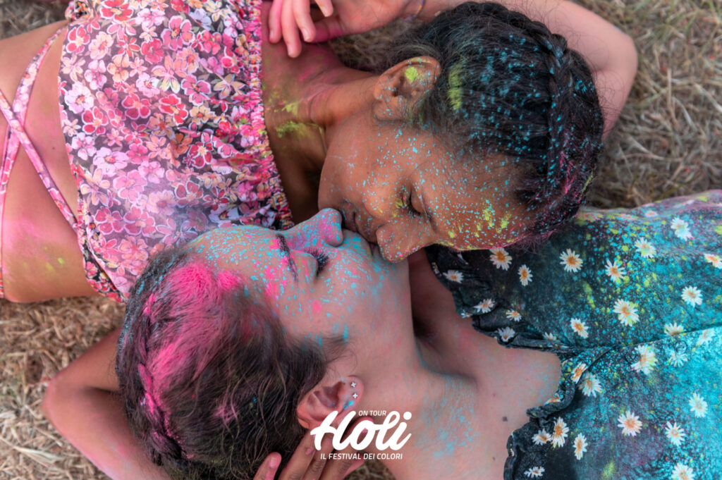 holi - Festival dei colori - un ragazzo e una ragazza si baciano . Sono coperti di colori e intorno a loro c'è una grossa folla sporca di colori