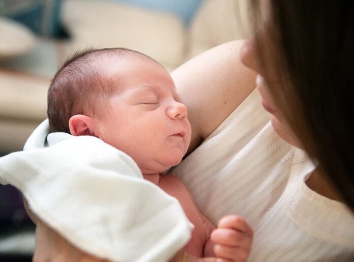 assistente materna - nella foto un neonato con gli occhi chiusi in braccio a una donna