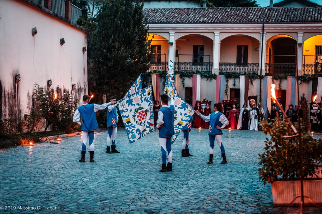 4 sbandieratori sventolano le bandiere del palio medievale e sono vestiti in abiti d'epoca del 400, in mezzo alla piazza del paese