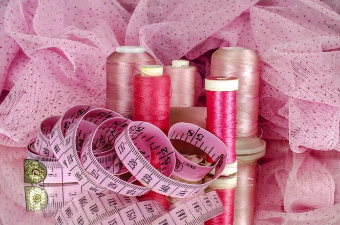moda sostenibile - su un tulle rosa sono appoggiati dei rocchetti di filo rosa e rosso e un metro da sarta rosa