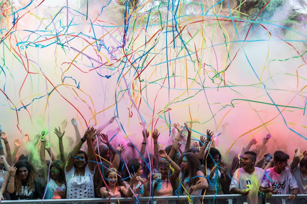 tanta gente sta festeggiando completamente ricoperta di color. Sopra di loro stelle filanti e polvere colorata