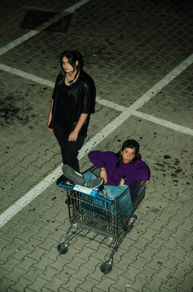 ventidue - nudda e chesma all'aperto, dentro un parcheggio, con una delle due cantanti seduta all'interno di un carrello da supermercato
