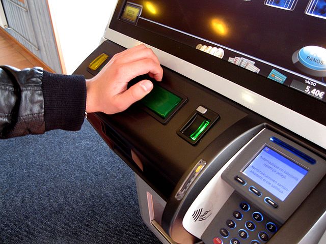 una mano che azione un pulsante di slot con bancomat vicino