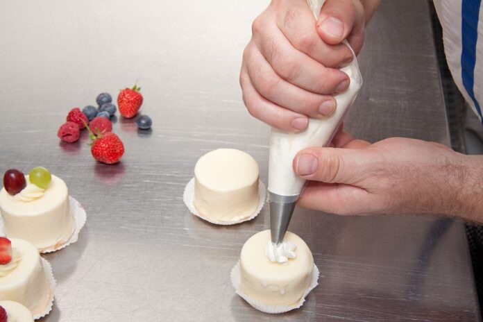 Belcolade Award 2023, un pasticcere sta creando un dolce al cioccolato bianco usando una sac a poche e vicino ci sono dei frutti di bosco rossi