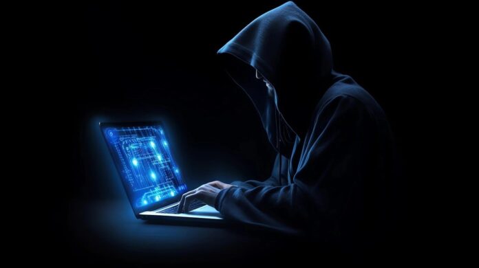 furto di identità - nella foto buia un pc con schermo blu e un tizio con un cappuccio sulla testa che sta operando una truffa on line