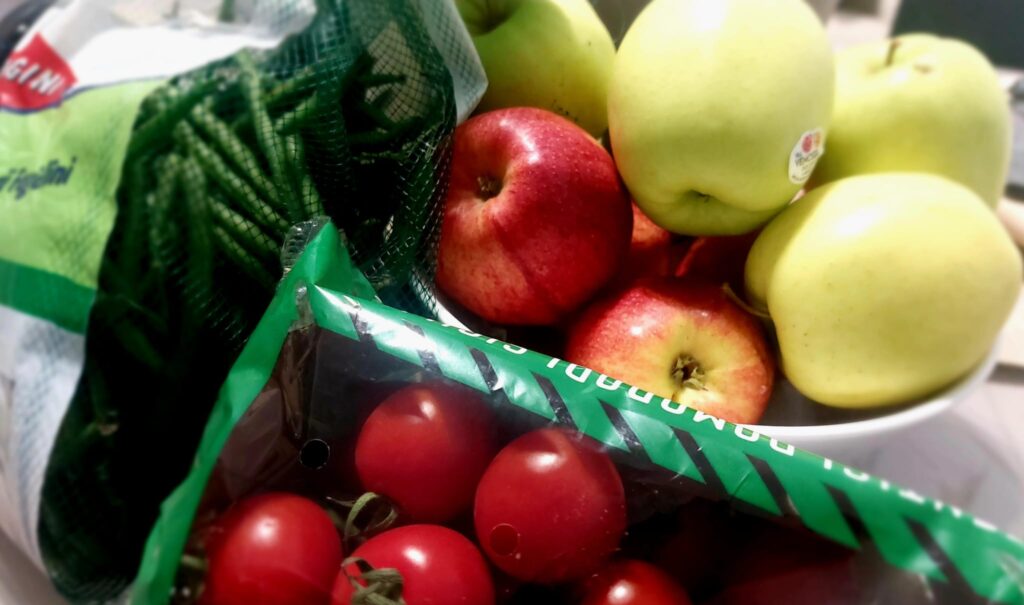 Imballaggi monouso per frutta e verdura - nella foto dei fagiolini in rete, dei pomodorini in vaschetta e delle mele rosse e gialle sfuse