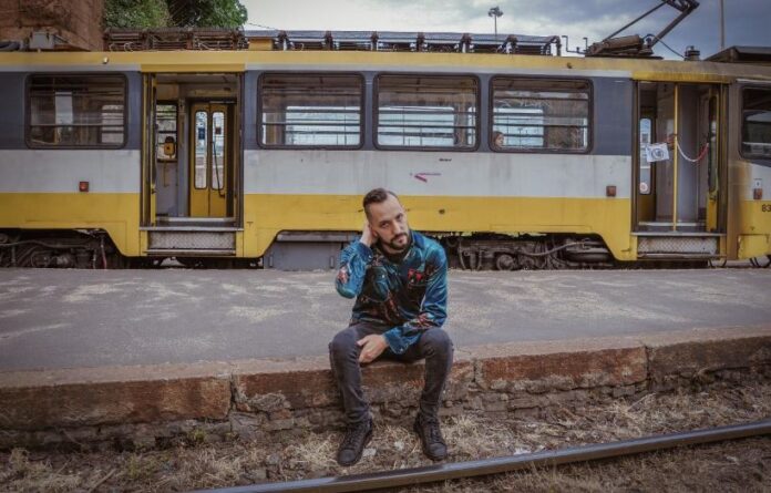 oggi - unfauno è seduto su un marciapiede, alle sue spalle vecchi tram bianchi e gialli