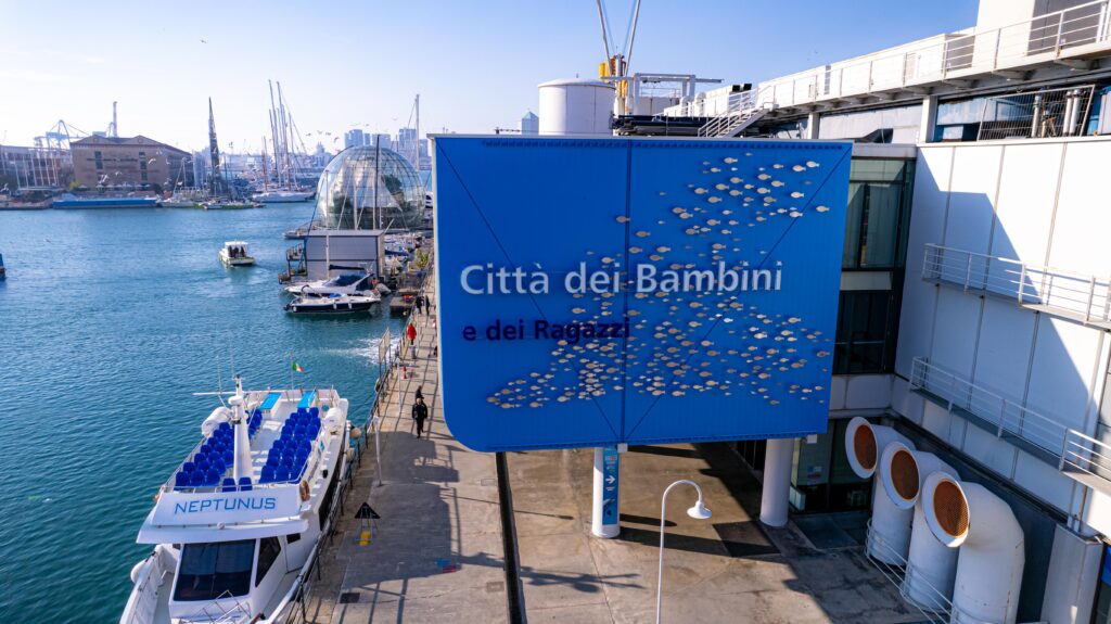 La città dei bambini e dei ragazzi - il cartellone azzurro sul molo del porto in cui si vedono delle imbarcazioni e il mare