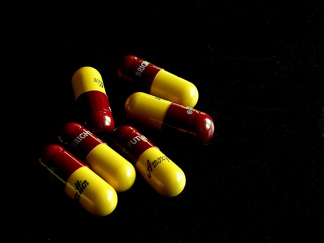 pillole di antibiotici in conezione gialla e  amaranto su fondo nero