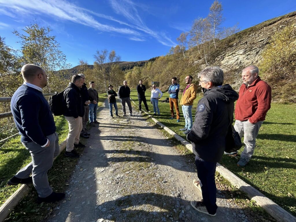 un gruppo di persone ai bordi di un sentiero di montagna con sullo sfondo le montagne e un cielo azzurro