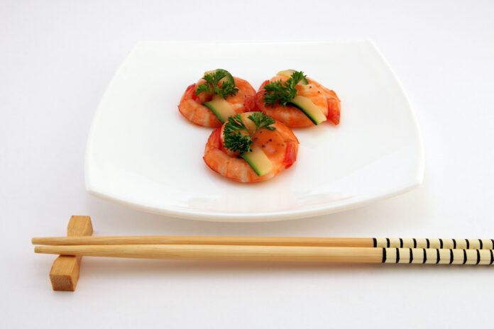 ristoranti cinesi e all you can eat - nella foto un piatto bianco con un'elegante disposizione di tre gamberi con del prezzemolo sopra e davanti al piatto due bacchette cinesi