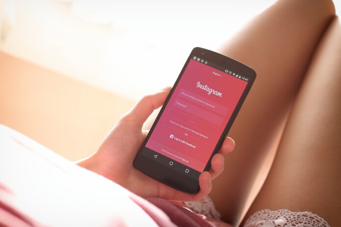 fake followers - una ragazza seduta su un letto ha in mano un telefonino con la schermata rossa su instagram