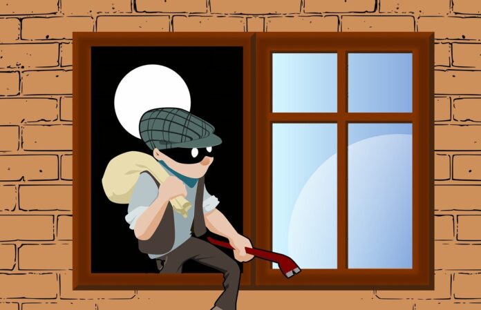 furto di casa - un fumetto che fa vedere un ladro con mascherina e coppola che con un sacco sulla spalla sta scavalcando una finestra per rubare in casa