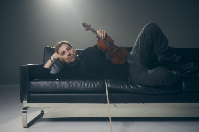 david garrett sdraiato su un divano di pelle nera, ha in mano un violino