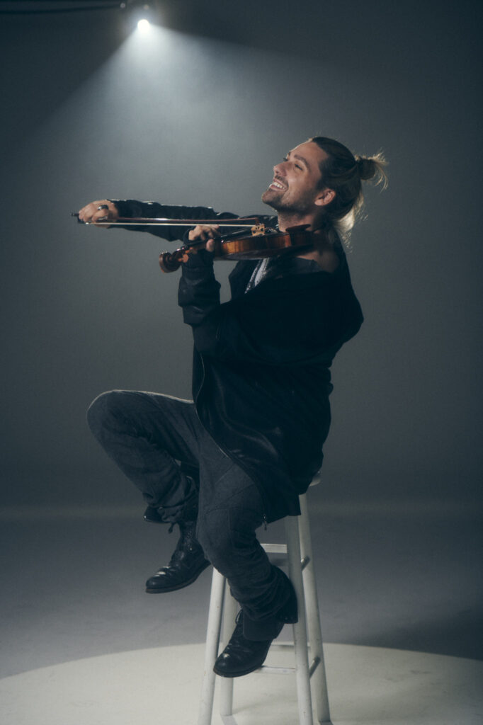 david garrett seguto su uno sgabello, intento a suonare il violino