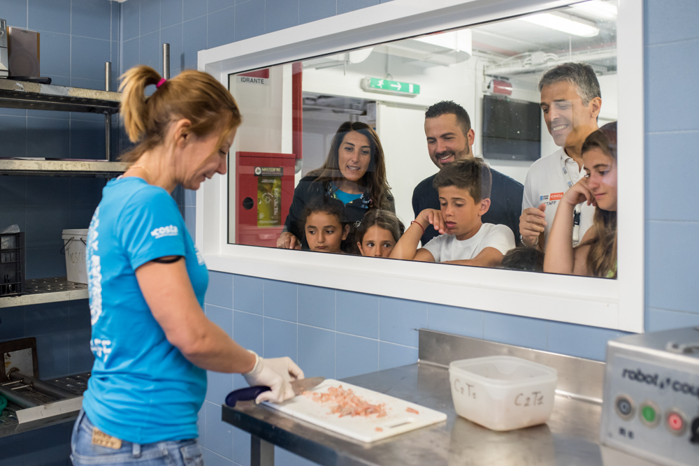 Acquario Village - un assitente dell'acquario sta preparando il cibo per i pesci e dietro ad un vetro ci osno delle persone che la stanno guardando