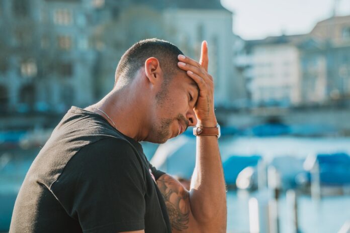 Dolore cronico - nella foto un uomo che indossa t shiret verde, ha capelli rasati e si tocca la fronte con la mano con espressione sofferente