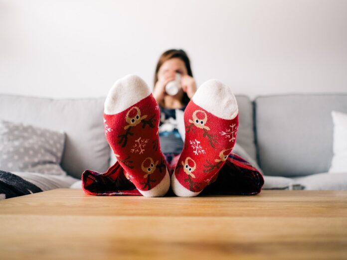 Stress da Natale - una donna è seduta sul letto e vbeve una tazza di the caldo. Indossa (in primo piano) calzini rossi con disegni natalizi