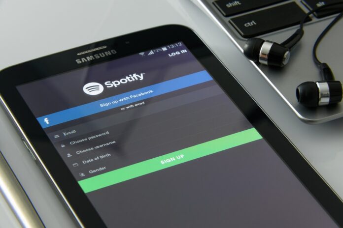 Spotify - la schermata di un cellulare sul sito di musica in streaming e vicino si vedono un paio di auricolari per ascoltare musica