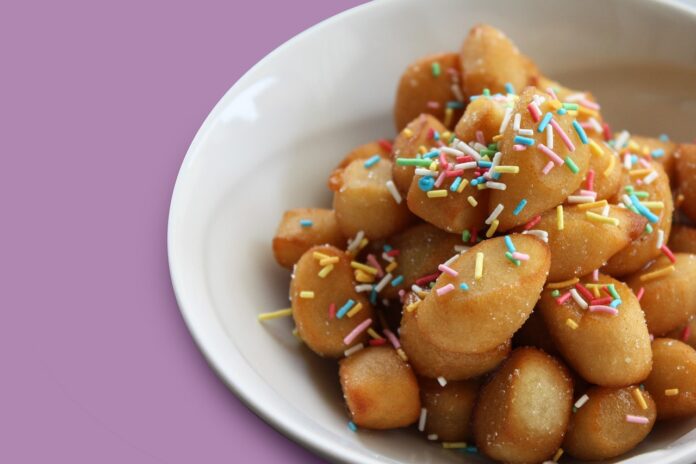 degli struffoli in un pistto bianco, coperti da granella colorata, sfondo rosa