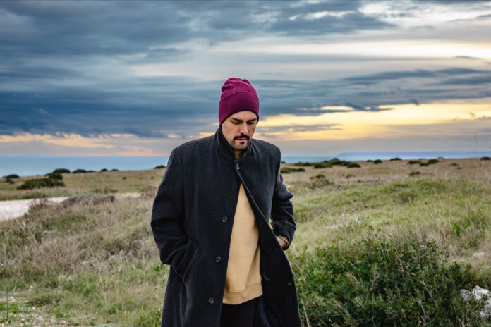 cortese fotografato all'aperto, indossa un cappotto scuro e un berretto di lana rossa