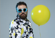 dargen d'amico indossa una giacca bianca a fiori neri e gialli, ha gli occhiali sa sole con la montatura azzurra e un palloncino giallo in mano