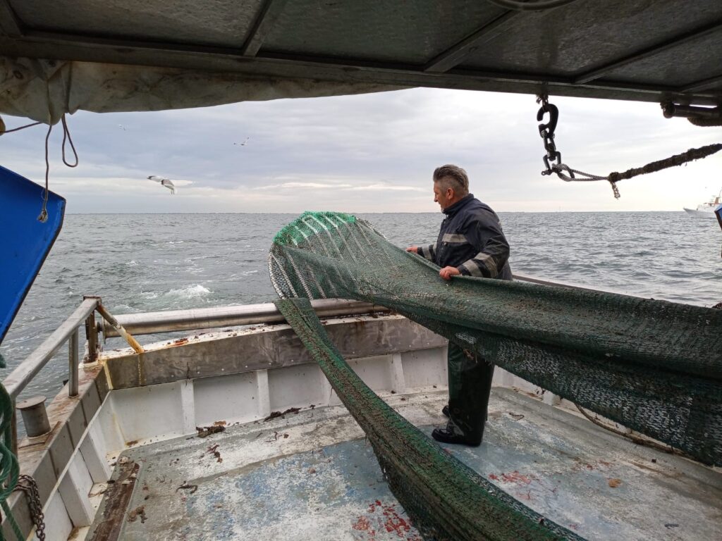 Un uomo su una barca in mezzo al mare sta tirando delle reti verdi