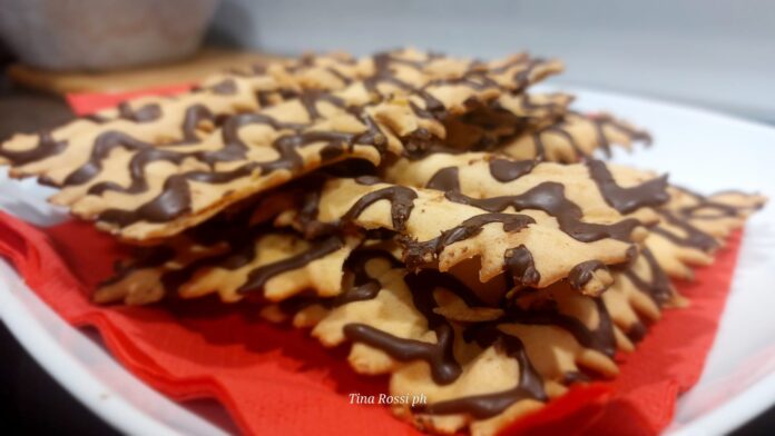 Chiacchiere di carnevale - dei dolci ricoperti di cioccolato appoggiate su un piatto bianco con un tovagliolorosso