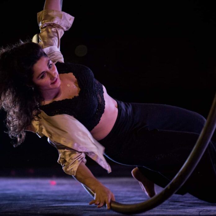 circo - una donna con una mano appoggiata in terra e l'altro braccio alzato verso l'alto, con le gambe distese sta saltando dentro a un cerchio