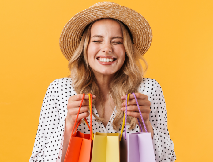 Promozioni e saldi - una donna bionda indossa un cappello a falda larga, una camicetta a pois, sorride felice e tiene in mano dello borse da shopping