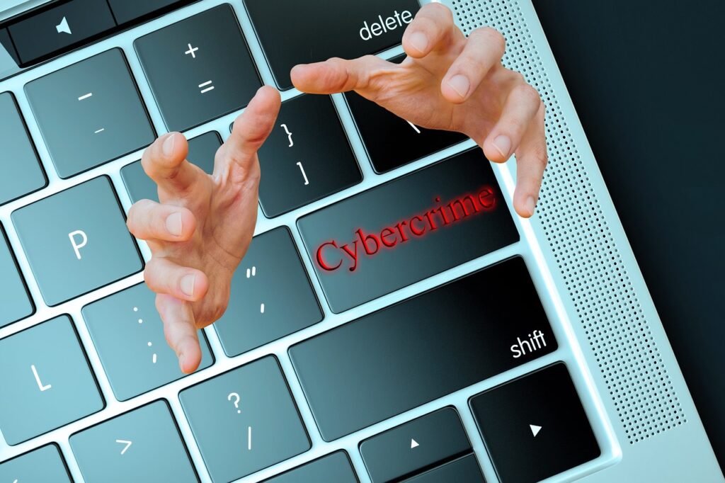 crimini informatici - una porzione di tastiera da pc dalla quale escono due mani e la parola "cybercrime"