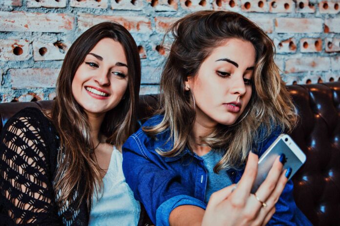 Influencer sui social - due ragazze con capelli lunghi sono sedute e si fanno un video con il cellulare