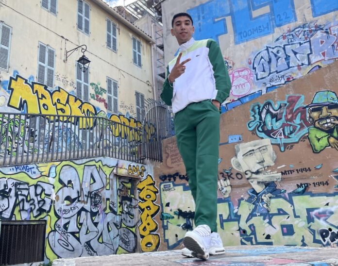 favela - 8blevrai all'aperto, circondato da murales, indossa una tuta biance e verde