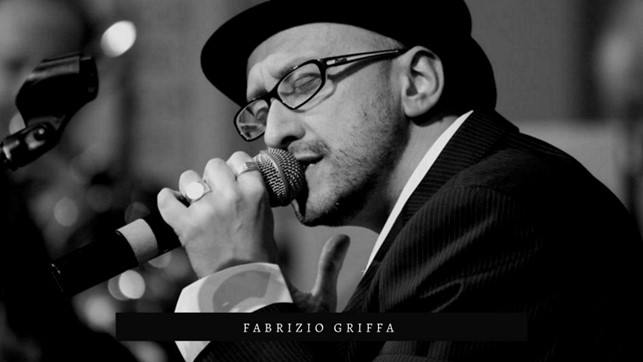 fabrizio Griffa in primo piano, indossa giacca e cappello neri