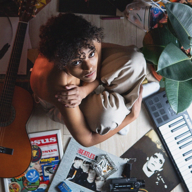 panorama - la copertina del nuovo singolo di kaze, che la ritrae inginocchiata sul pavimento, circondata da disci e strumenti musicali