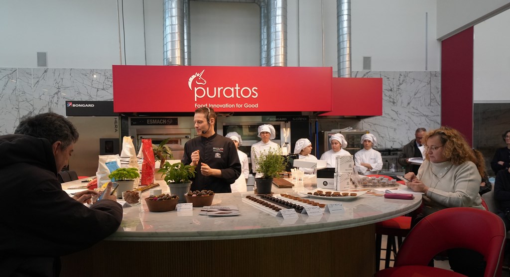 Puratos - uno chef con divisa nera, archetto di microfono in testa, sta tenendo una lezione con gente seduta ad un tavolo rotondo