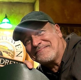 Enzo DEcaro indossa un cappellino con visiera verde, maglia scura, ha barba bianca incolta e sorride