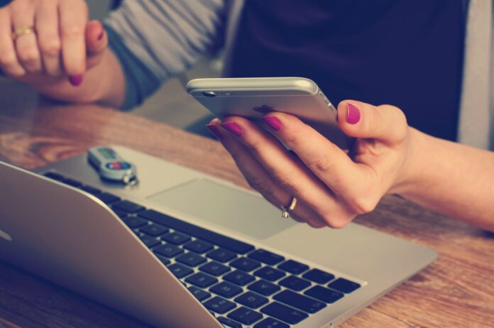 Truffe telefoniche - una mano di donna tiene un cellulare e davanti a lei c'è un pc portatile con la chiavetta di una banca