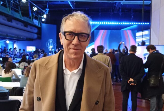Sanremo 2024 - nella foto il Sindaco Alberto Biancheri che indossa cappotto beige, occhiali , giacca nera, camicia bianca, ha i capelli grigi ed è nel teatro Ariston con tanta gente dietro