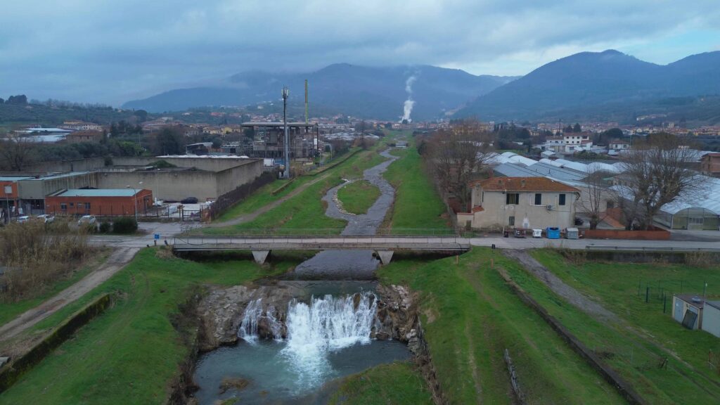 Contaminazione da PFAS - una veduta dall'alto degli scarichi fognari in un fiume circondato da argini verdi e case 